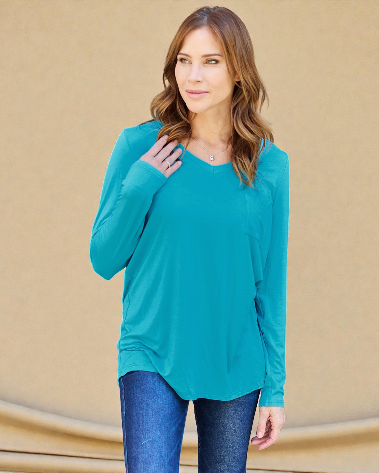 Woman wearing a teal long-sleeve top against a beige background