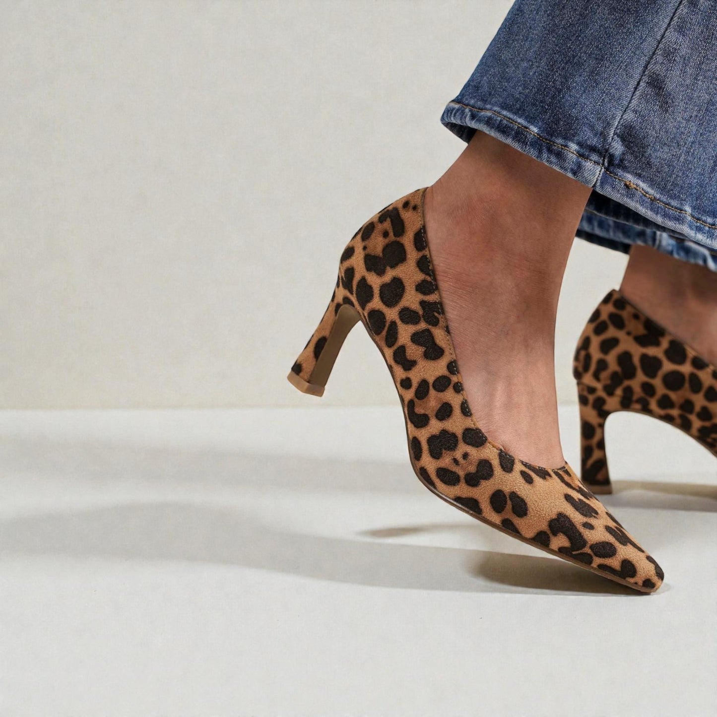 Leopard print high heels worn with a denim skirt on a neutral background