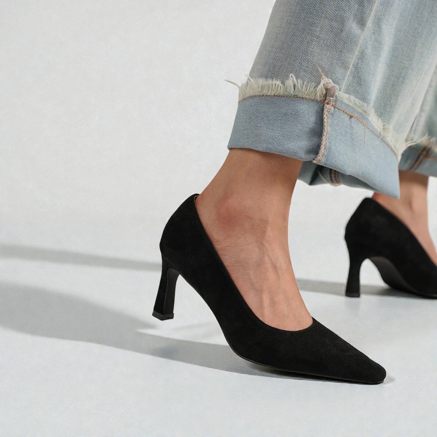 Black high-heeled shoes worn with light blue jeans on a white background