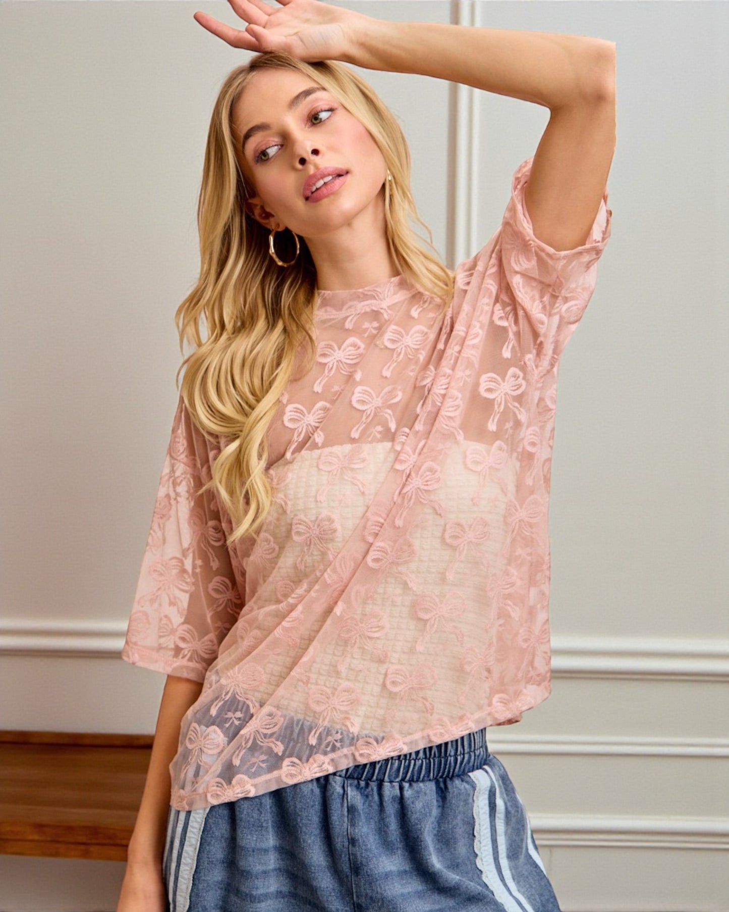 Woman wearing a pink lace top and blue shorts indoors.