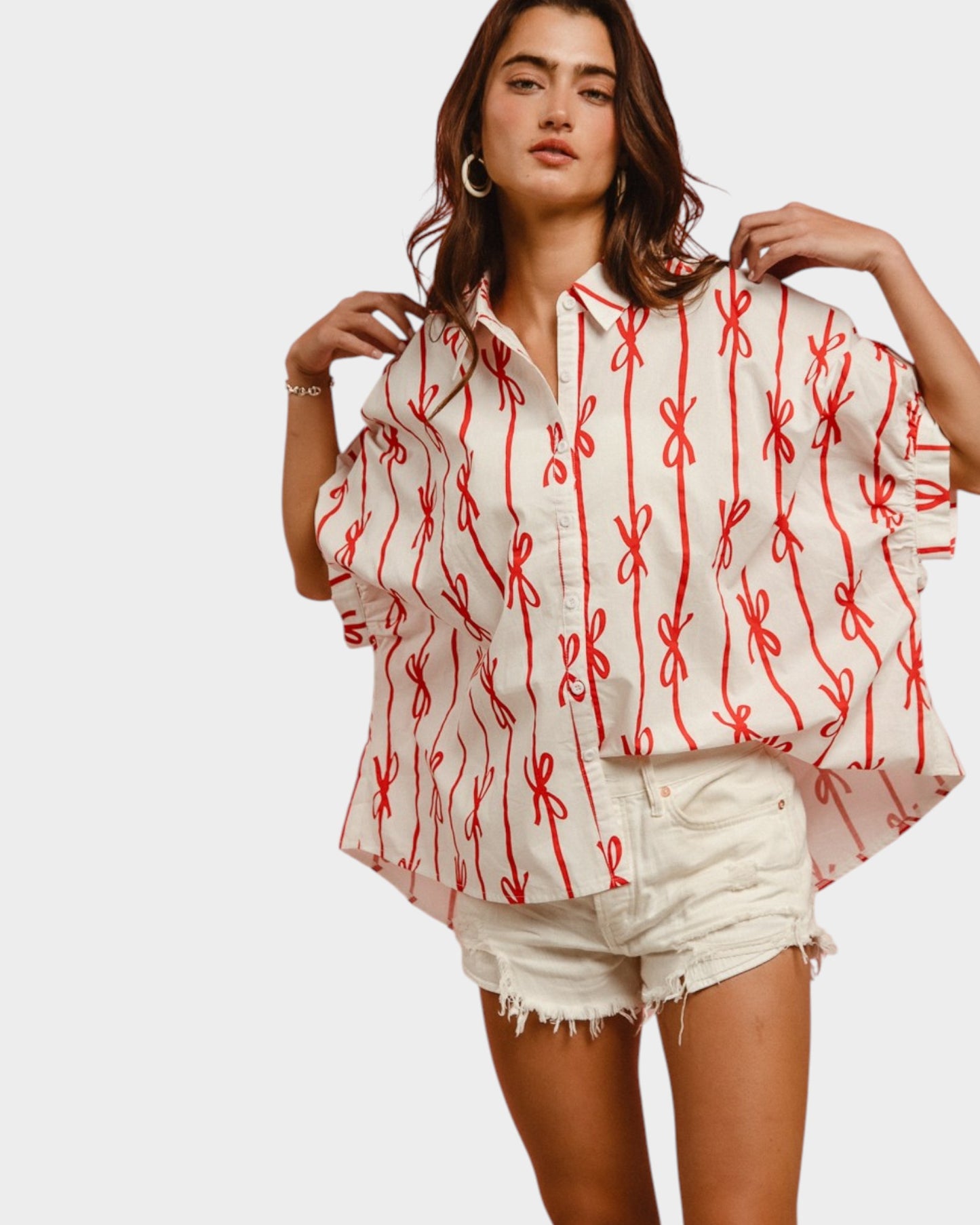 Woman wearing a white blouse with red patterns and denim shorts on a plain background