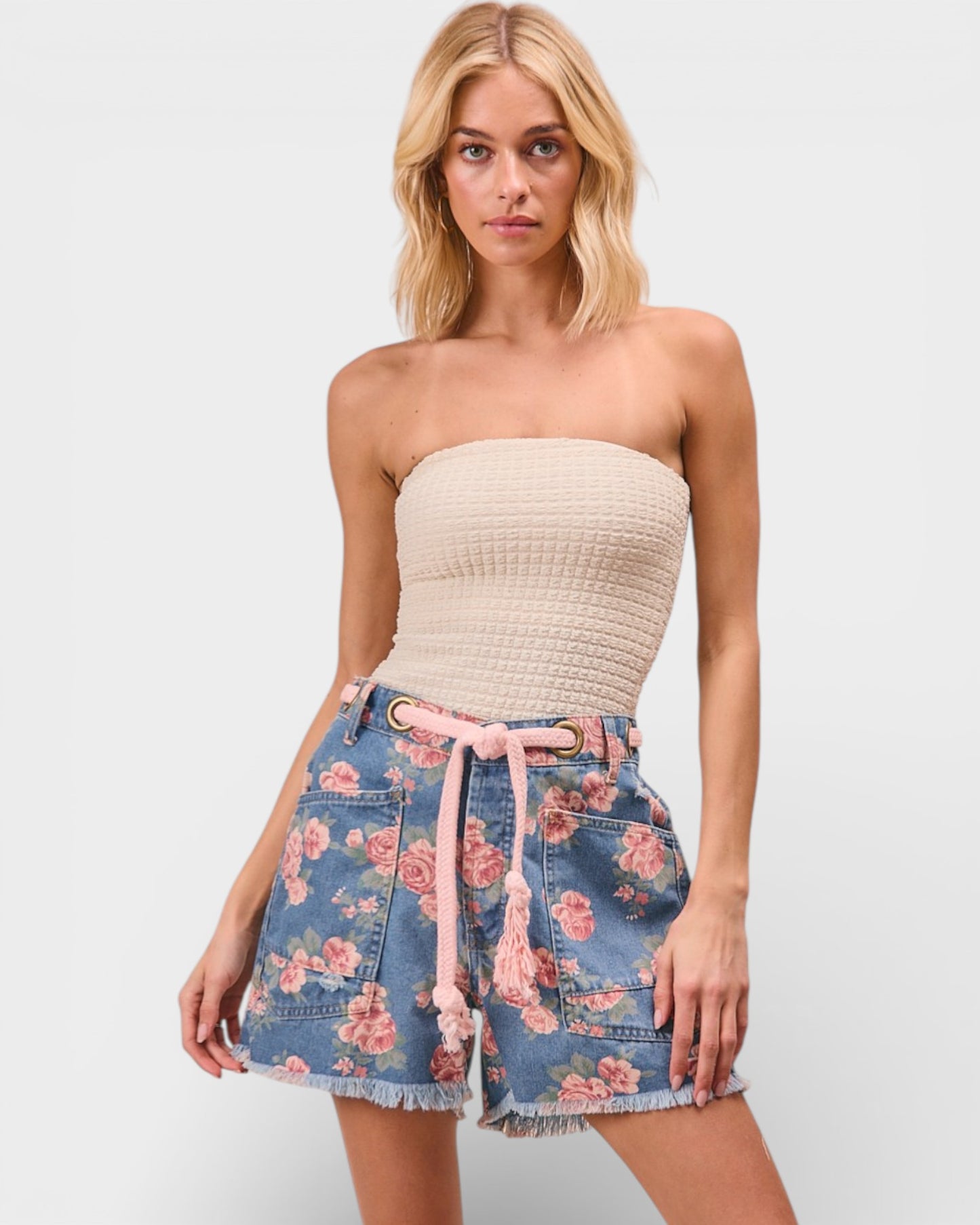 Woman wearing a strapless beige top and floral denim shorts on a white background
