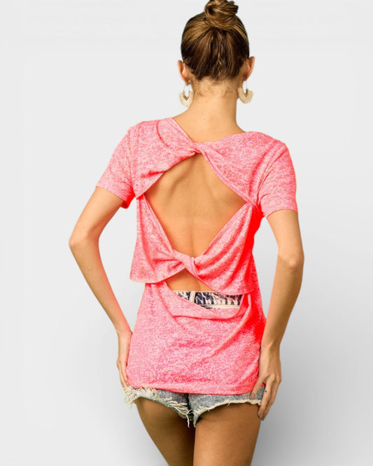 Woman wearing a pink open-back top and shorts on a plain background