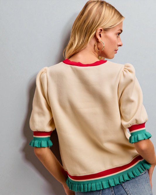 Woman wearing a beige sweater with colorful trim against a gray background