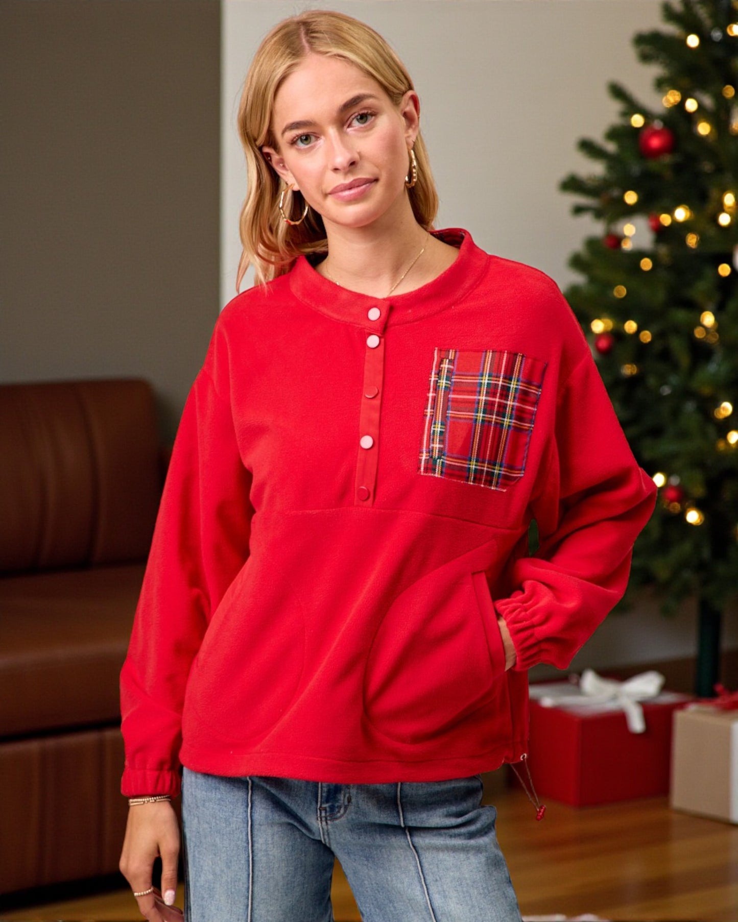 Person wearing a red long-sleeve shirt with a plaid pocket in front of a decorated Christmas tree.