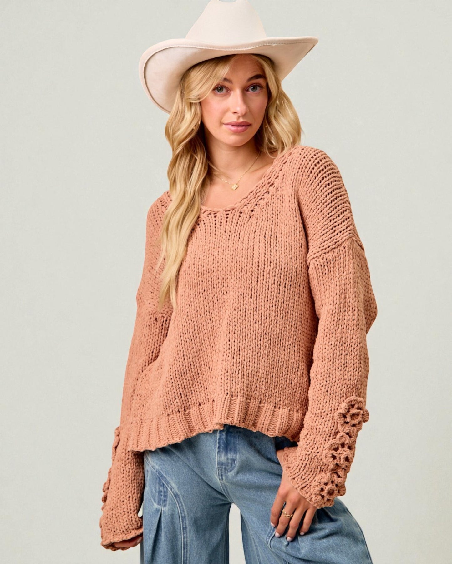 Woman wearing a pink knit sweater and wide-brimmed hat on a plain background