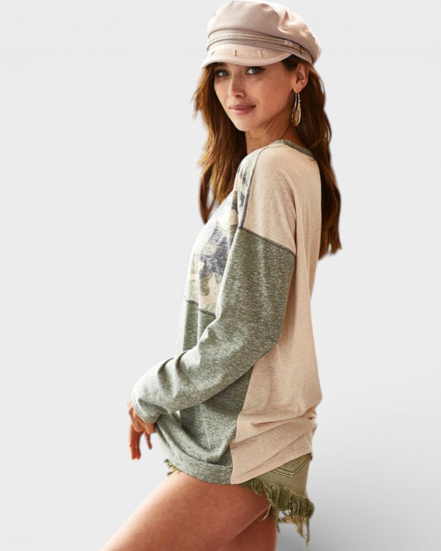Woman wearing a beige and green long-sleeve top with a cap on a white background