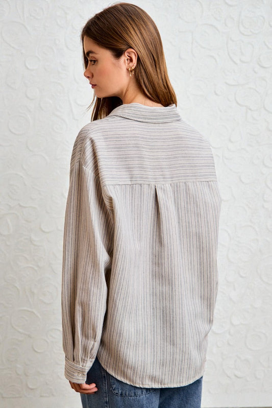 Woman wearing a light gray striped shirt against a white textured wall
