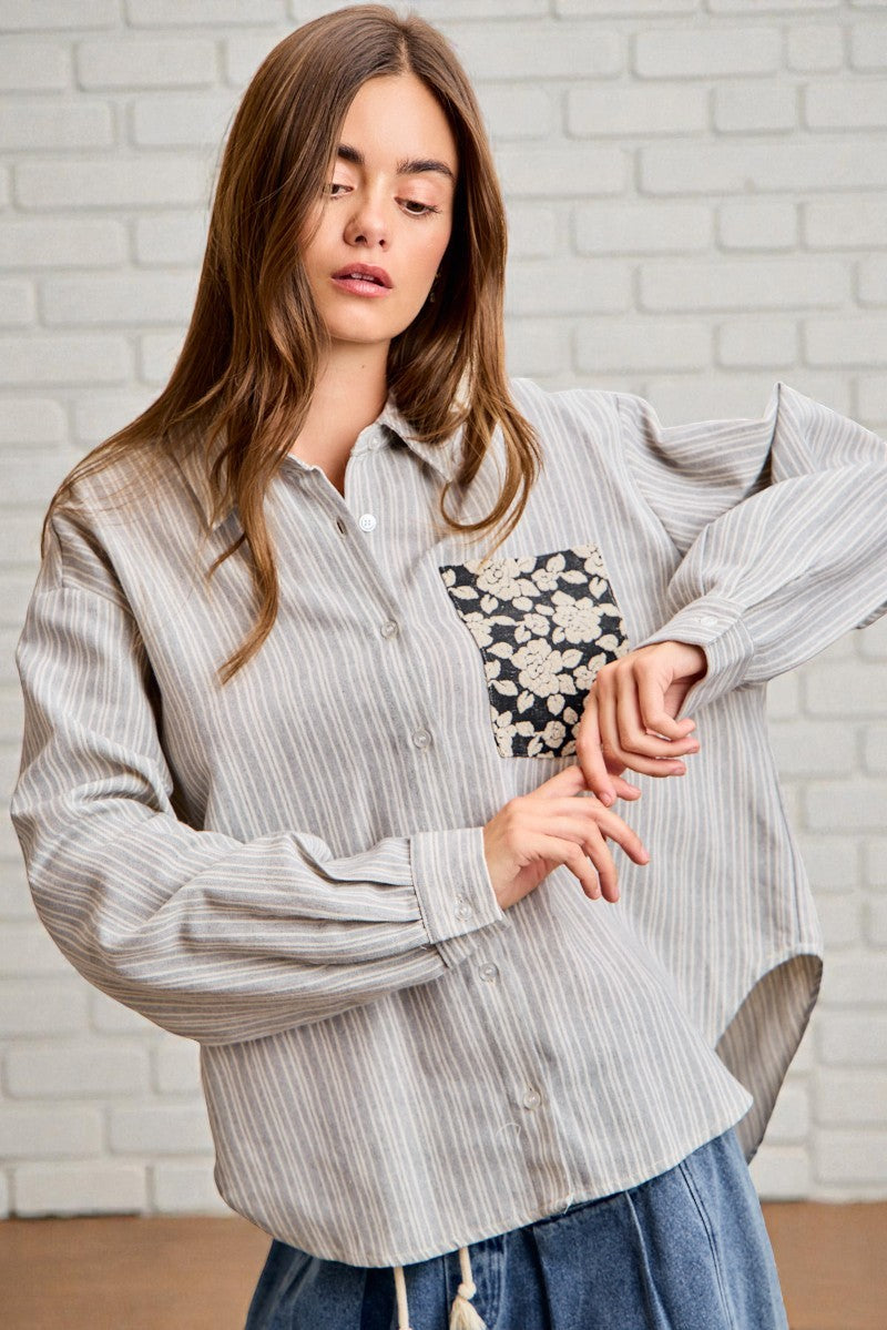 Woman wearing a striped shirt with a floral design in front of a white brick wall.