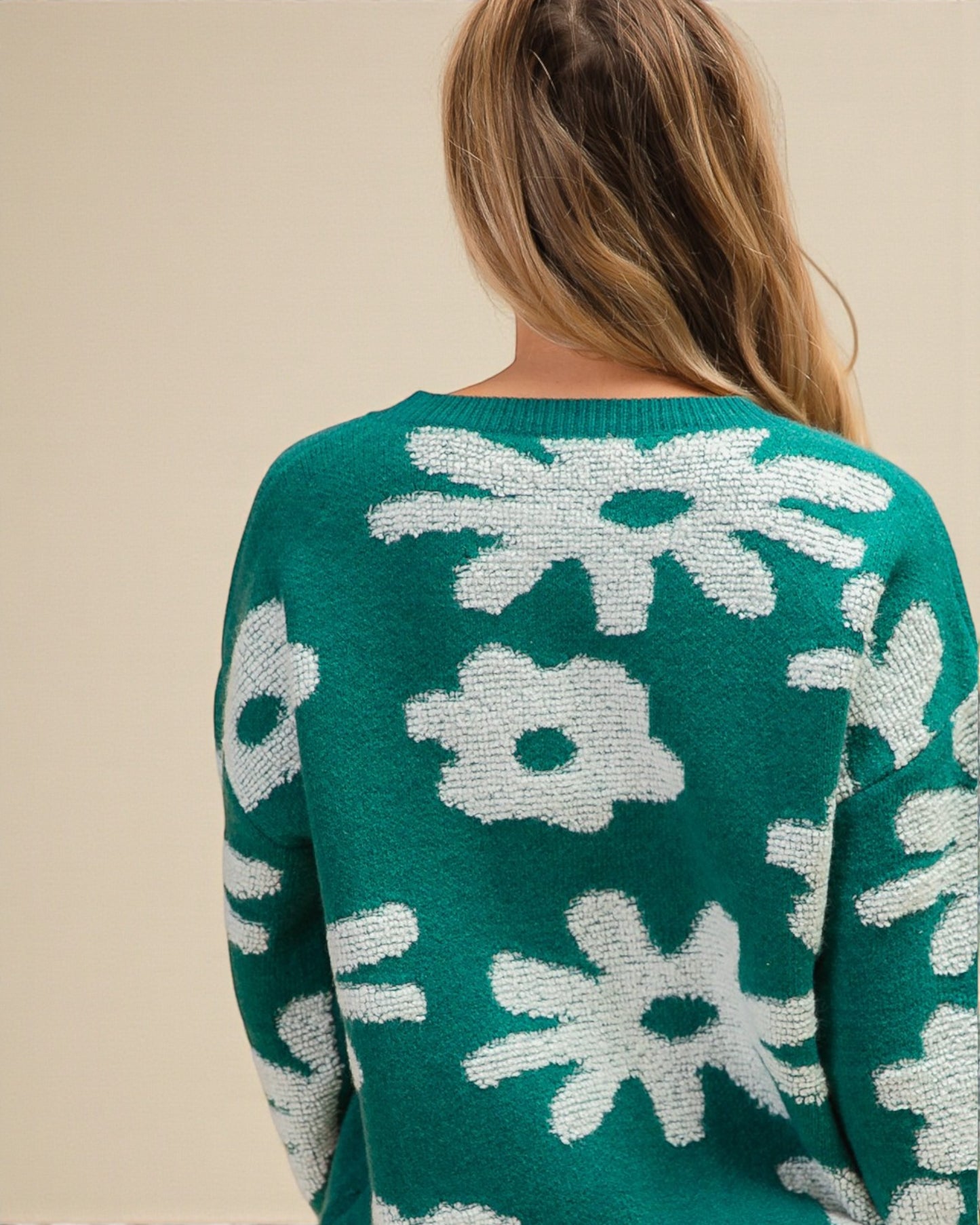 Green sweater with white floral patterns worn by a person on a beige background