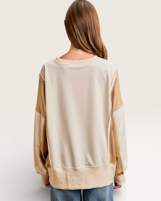 Person wearing a beige and brown color-blocked sweater on a plain background