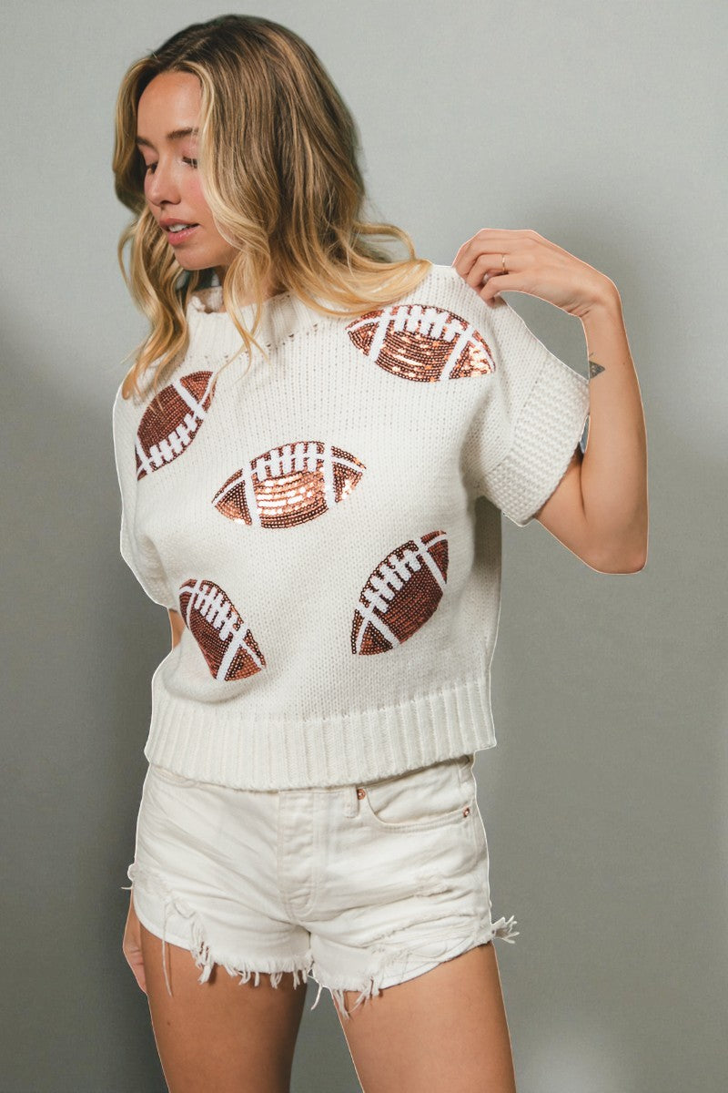 Woman wearing a white sweater with football patterns and white shorts against a gray background