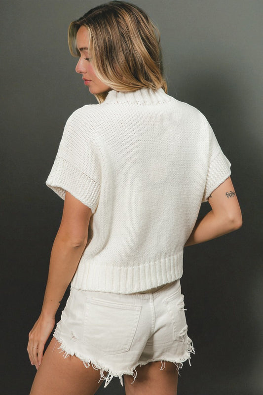 Woman wearing a white knit top and shorts against a dark background