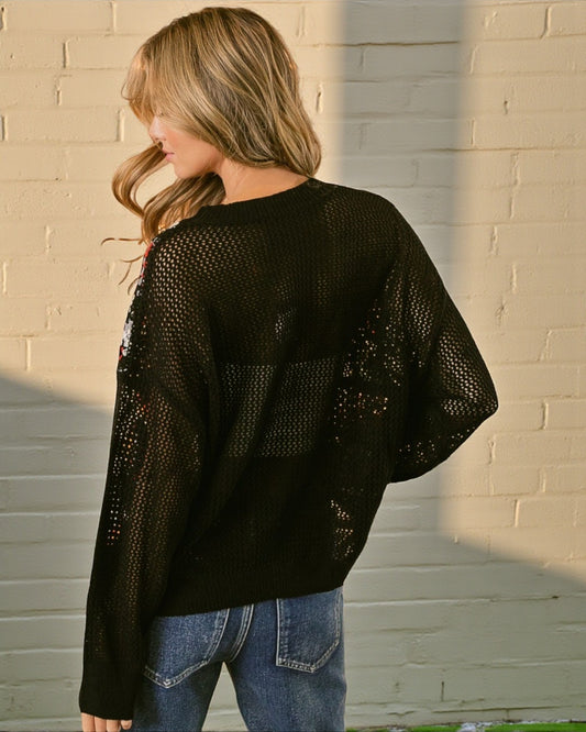 Person wearing a black sequin sweater against a beige brick wall.