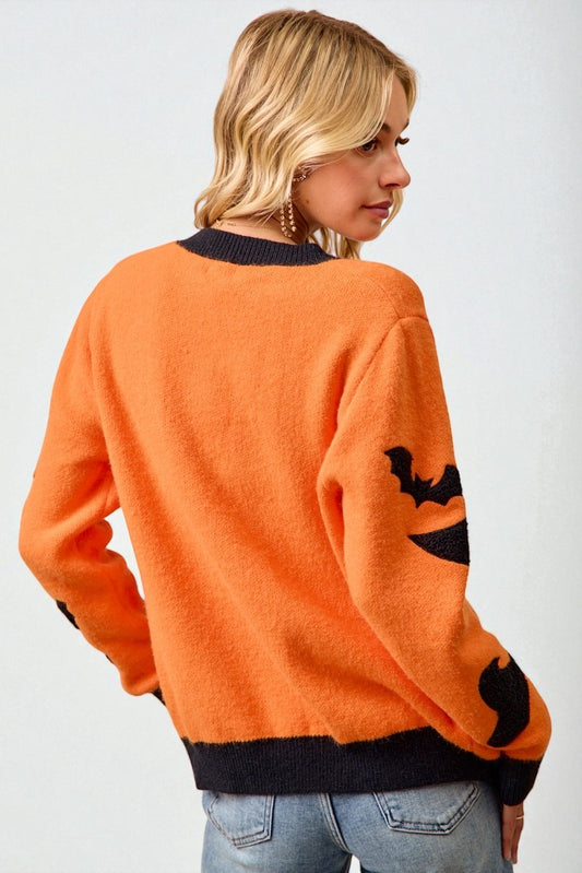 Person wearing an orange sweater with black cat designs on a plain background