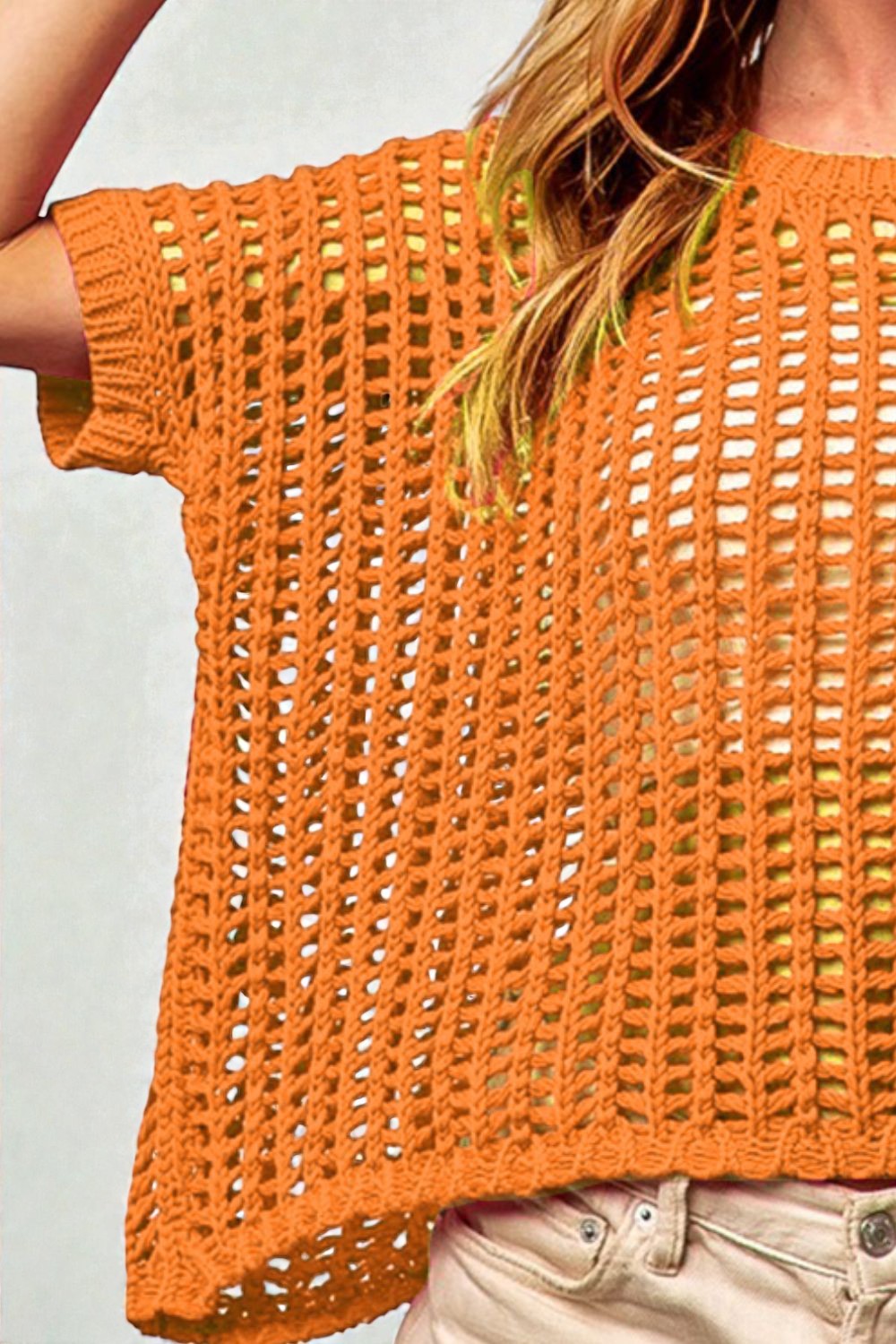 Orange crochet top worn by a person on a plain background
