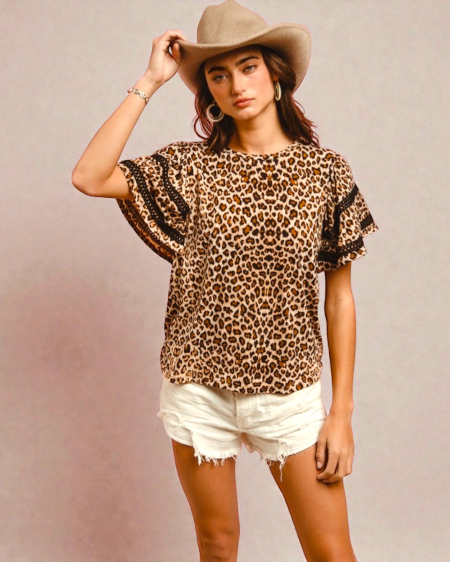 Woman wearing a leopard print top with ruffled sleeves and white shorts against a plain background