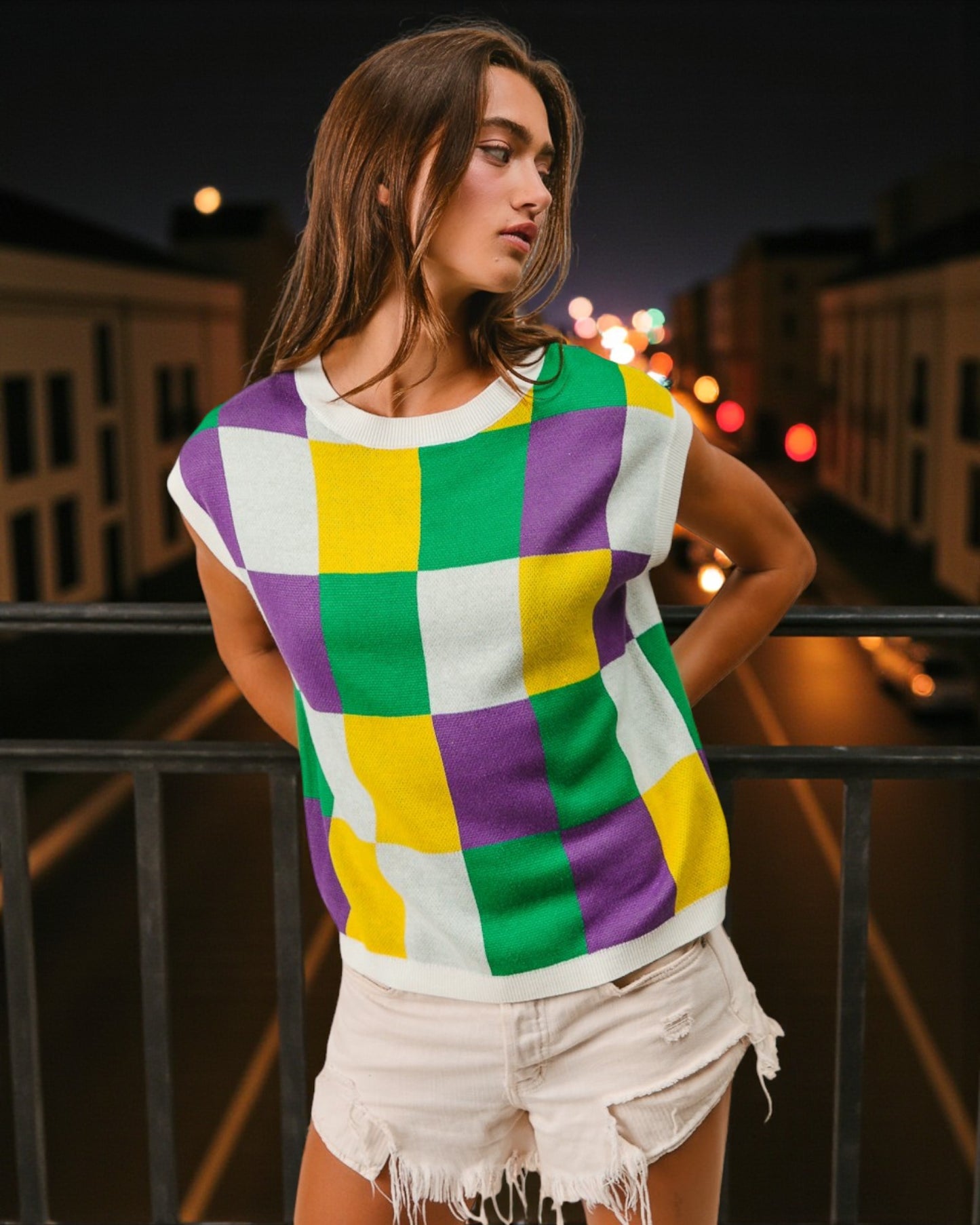 Woman wearing a colorful checkered shirt with a cityscape background at night.
