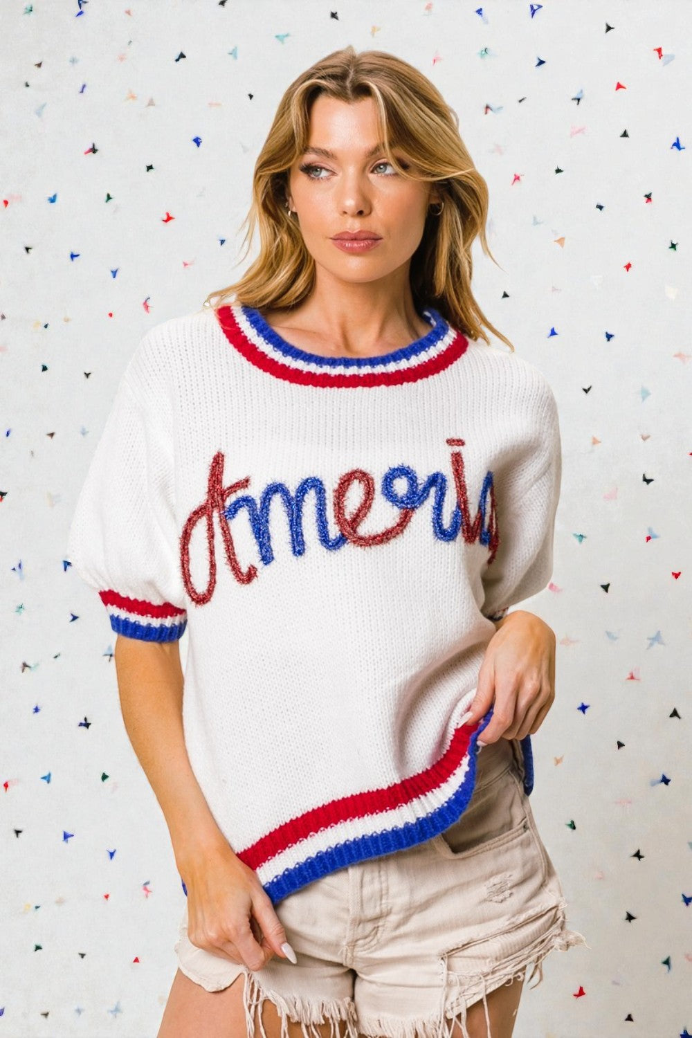 Woman wearing a white sweater with red and blue accents against a multicolored dot pattern background