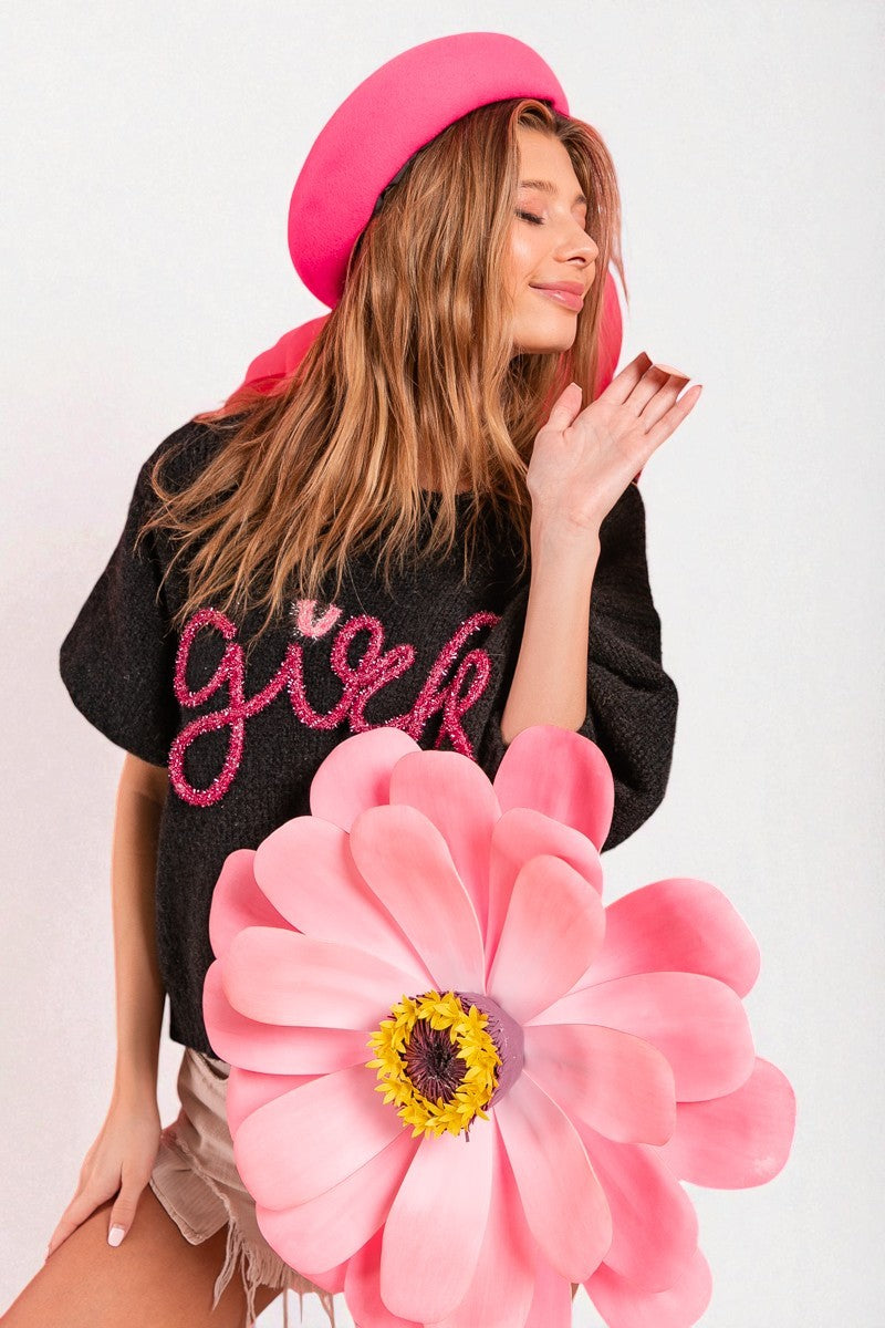 Woman wearing a black jacket with pink text, holding a large pink flower against a white background