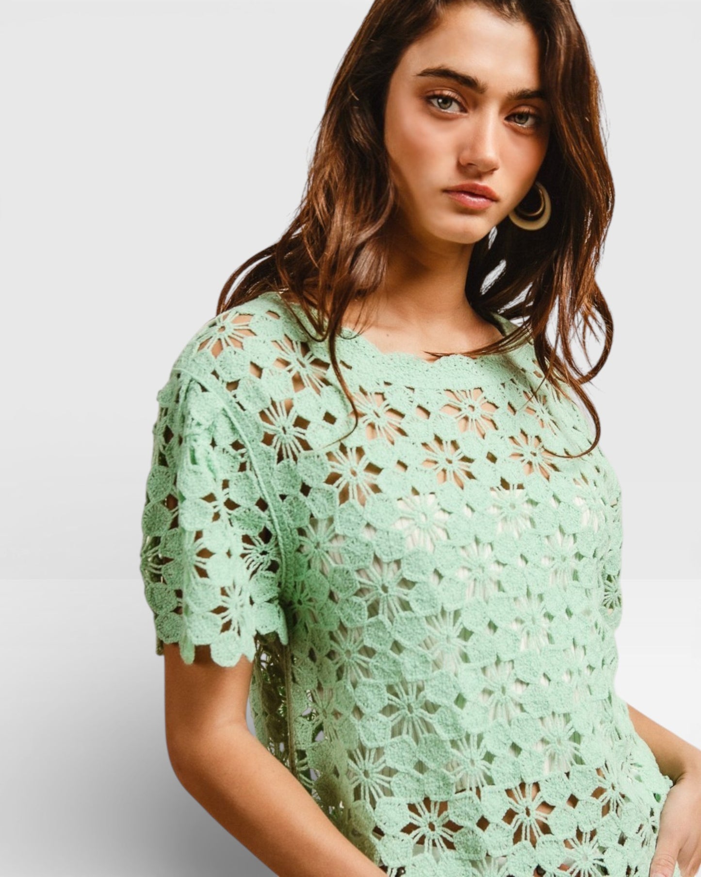 Woman wearing a light green lace top against a plain background