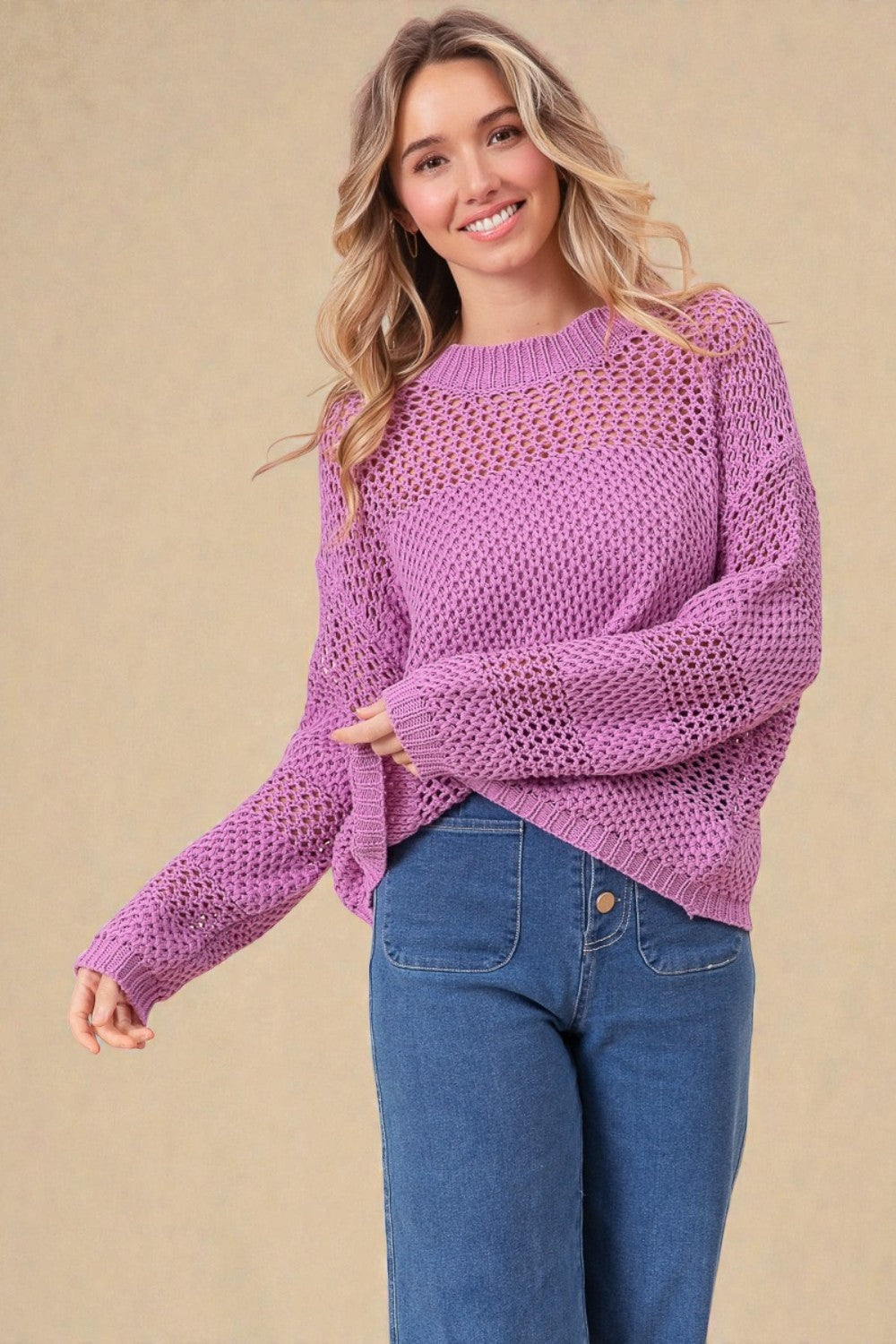 Woman wearing a purple sweater and blue jeans against a beige background