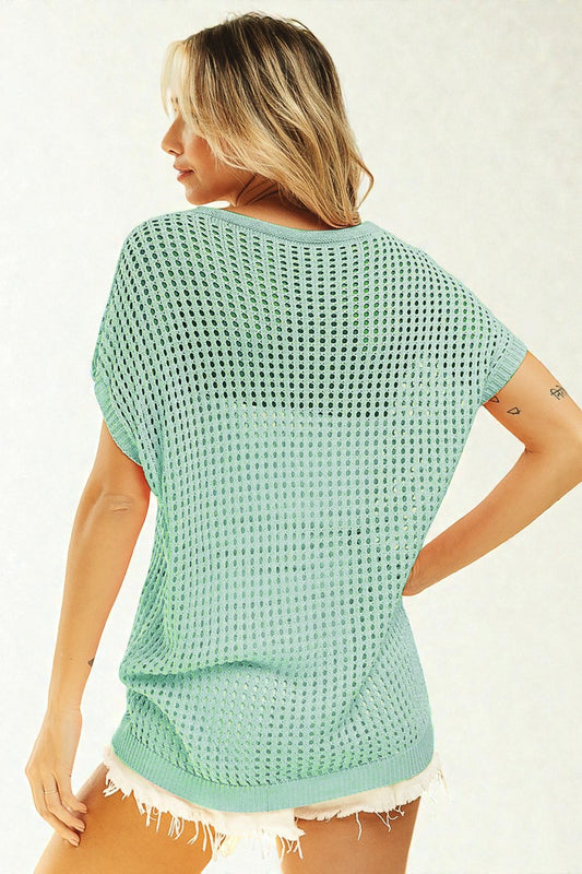 Woman wearing a light green textured top and white shorts on a plain background