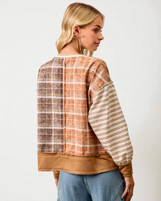 Woman wearing a plaid and striped long-sleeve top with a plain background