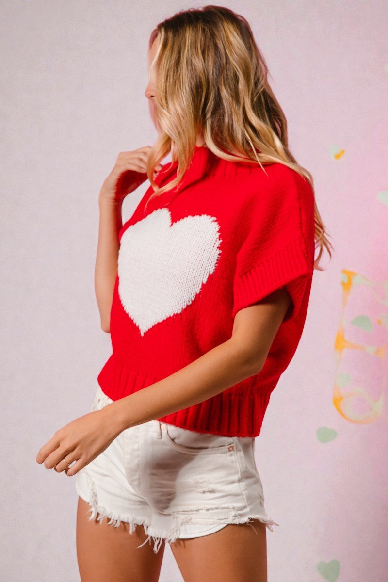Woman wearing a red sweater with a white heart design against a light pink background.