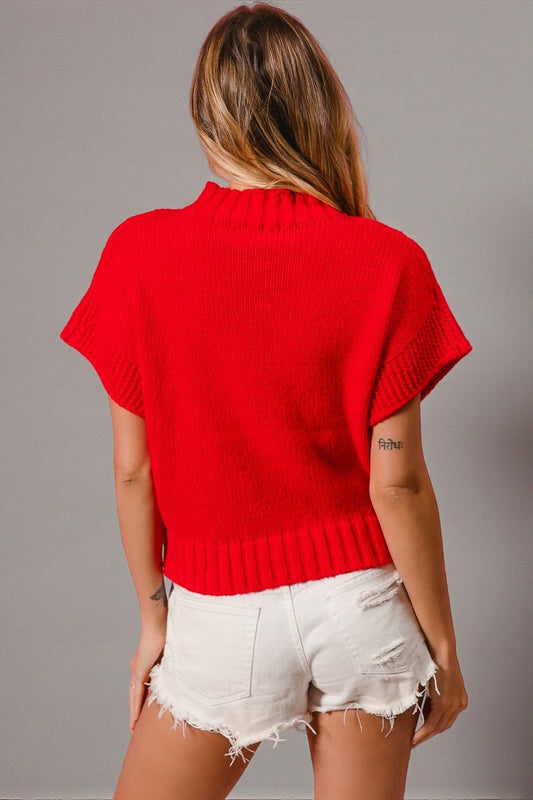 Person wearing a red sweater and white shorts against a gray background