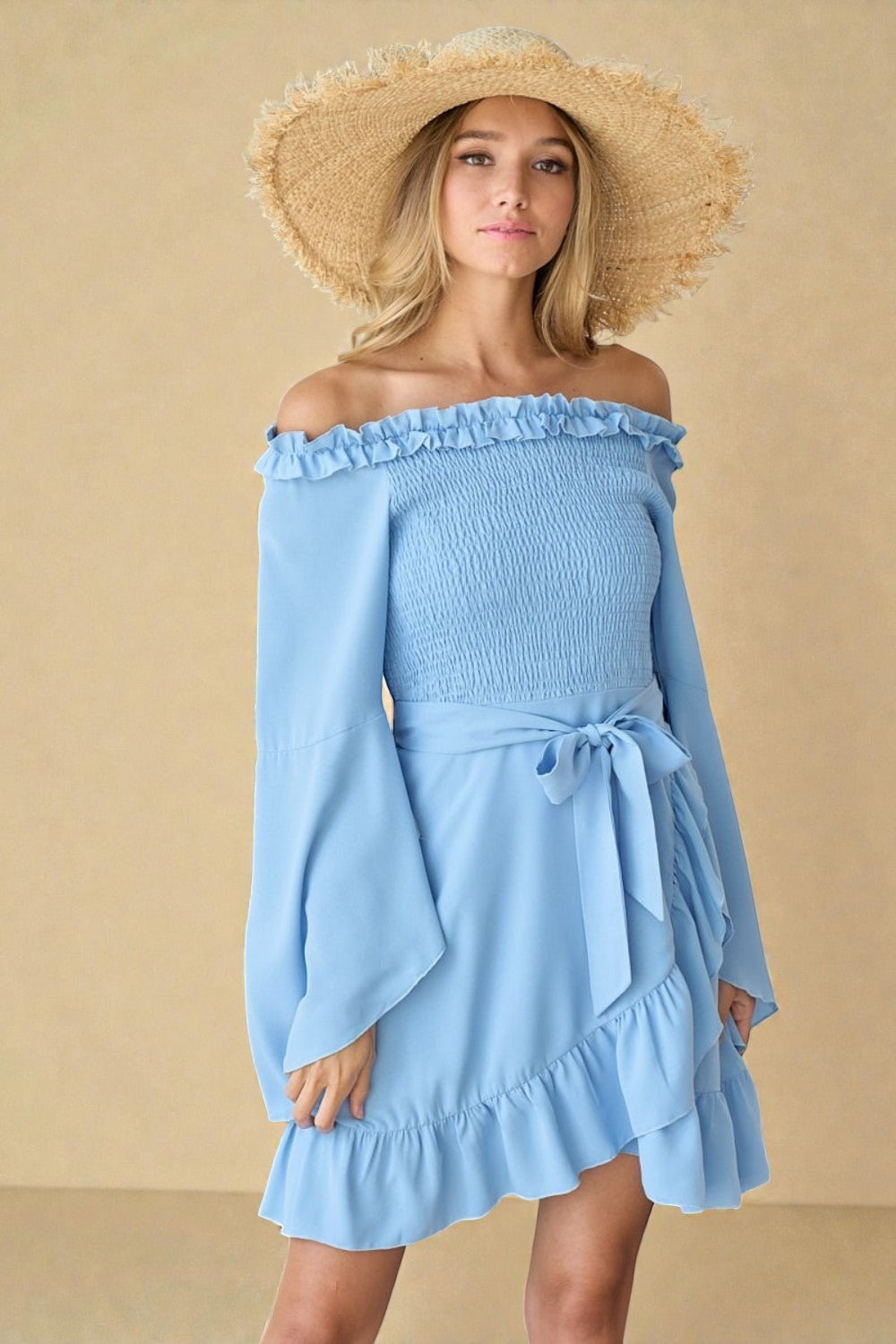 Woman wearing a light blue off-shoulder dress with long sleeves and a straw hat on a beige background
