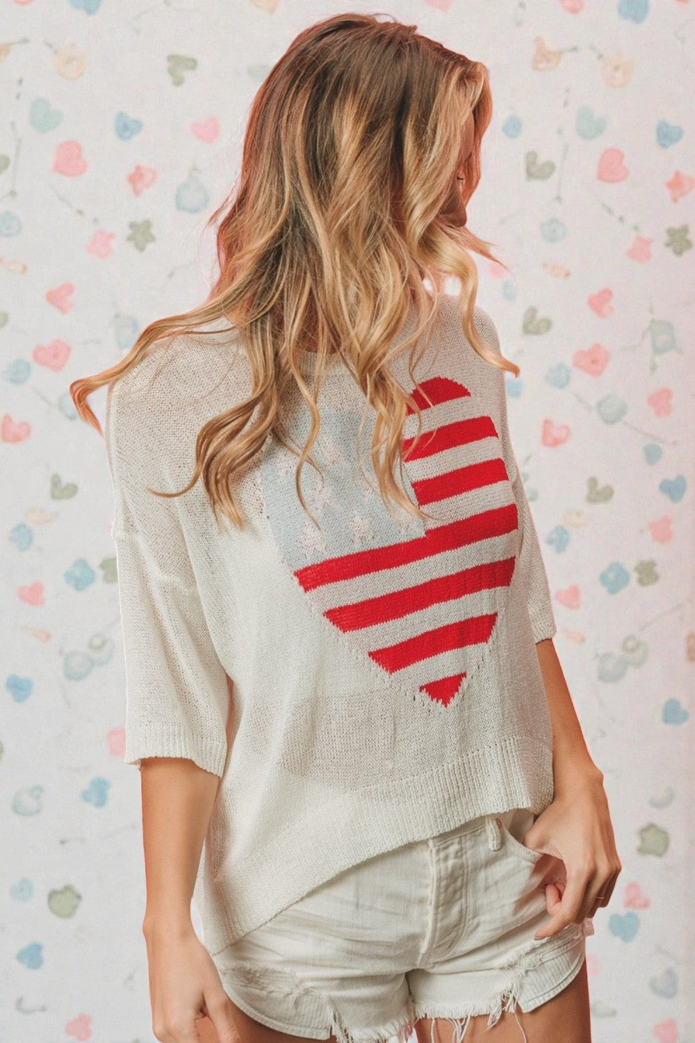 Person wearing a white sweater with a red heart design on a patterned background