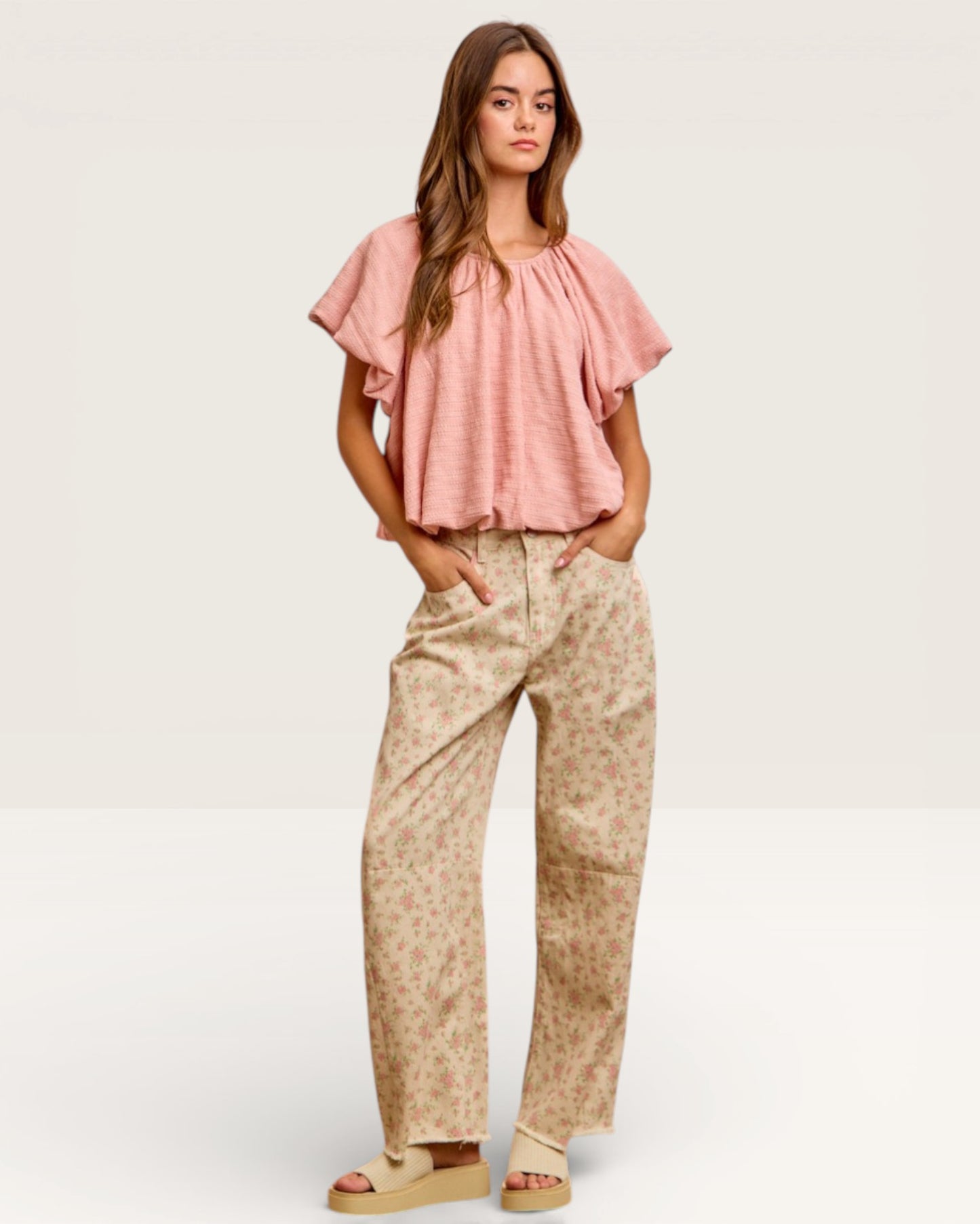 Woman wearing a pink blouse and beige patterned pants on a white background