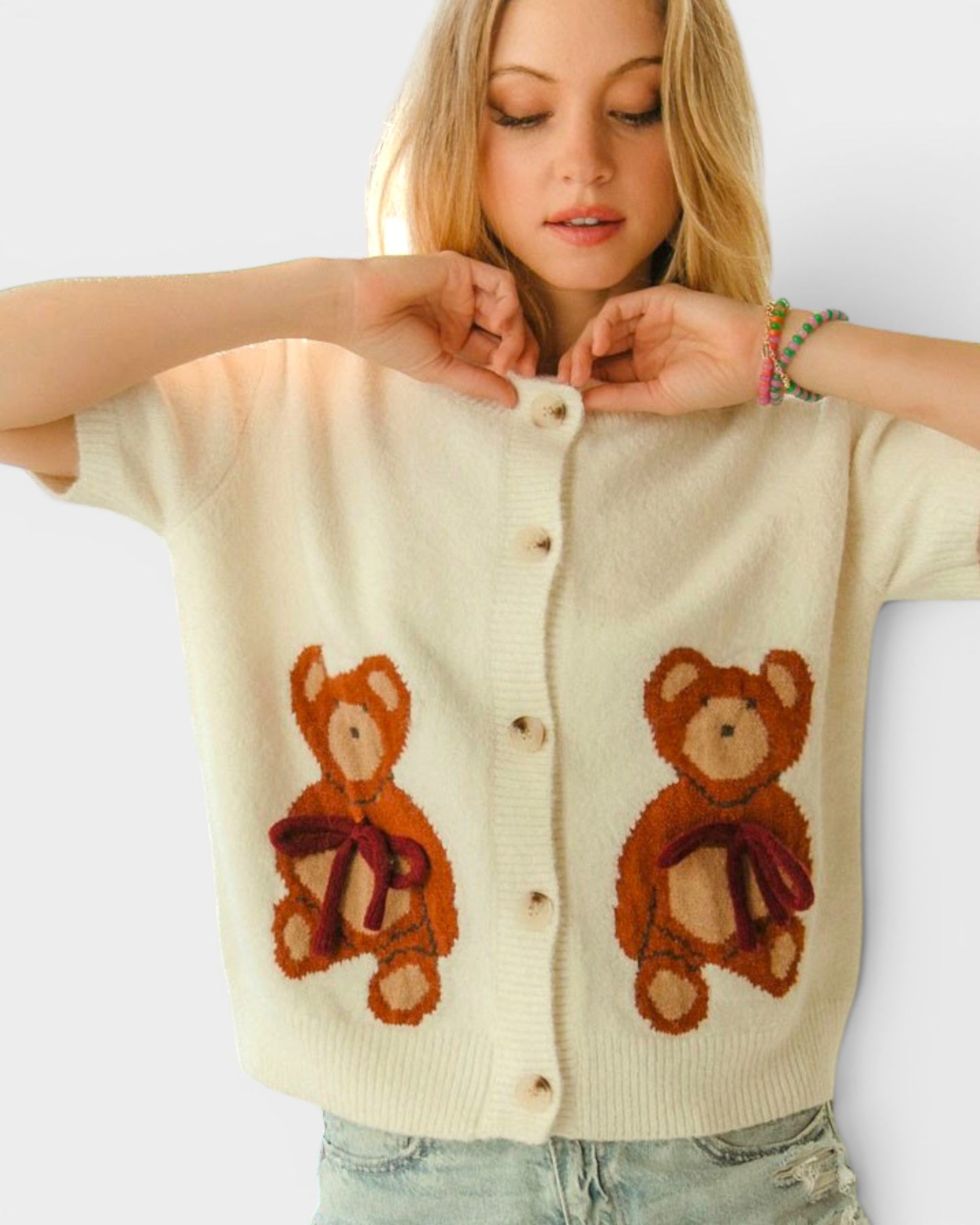 Woman wearing a cream-colored cardigan with teddy bear designs on a white background