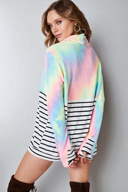 Woman wearing a colorful tie-dye poncho over a striped dress on a plain background