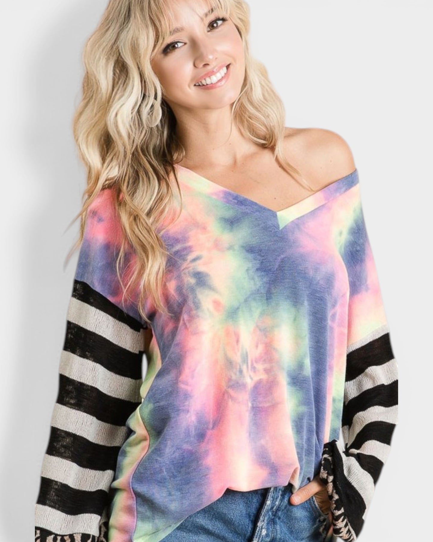Woman wearing a colorful tie-dye sweater with black and white striped sleeves on a plain background
