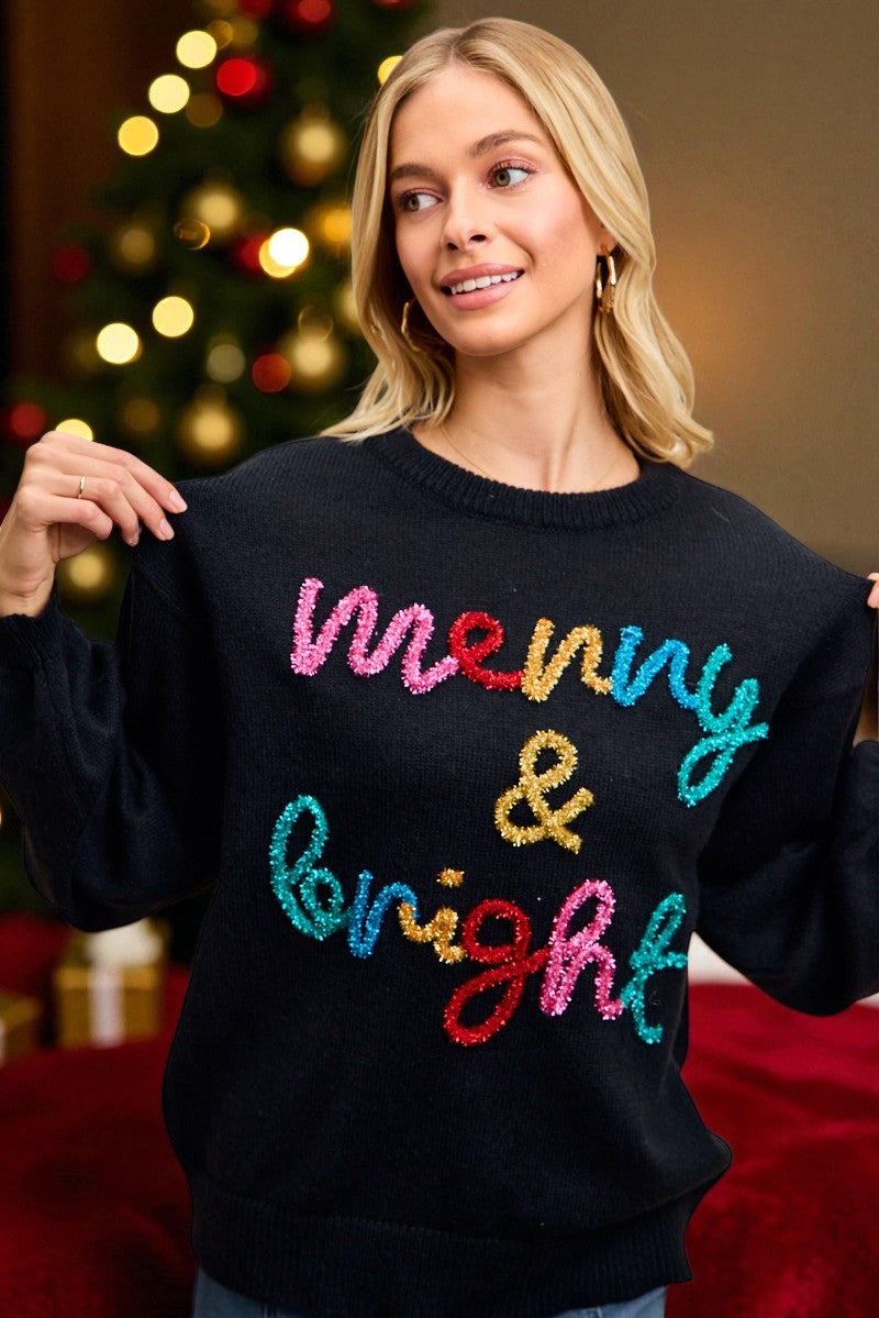 Woman wearing a black sweater with colorful text in front of a Christmas tree.