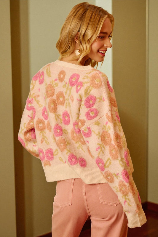 Woman wearing a floral patterned sweater and pink pants indoors.