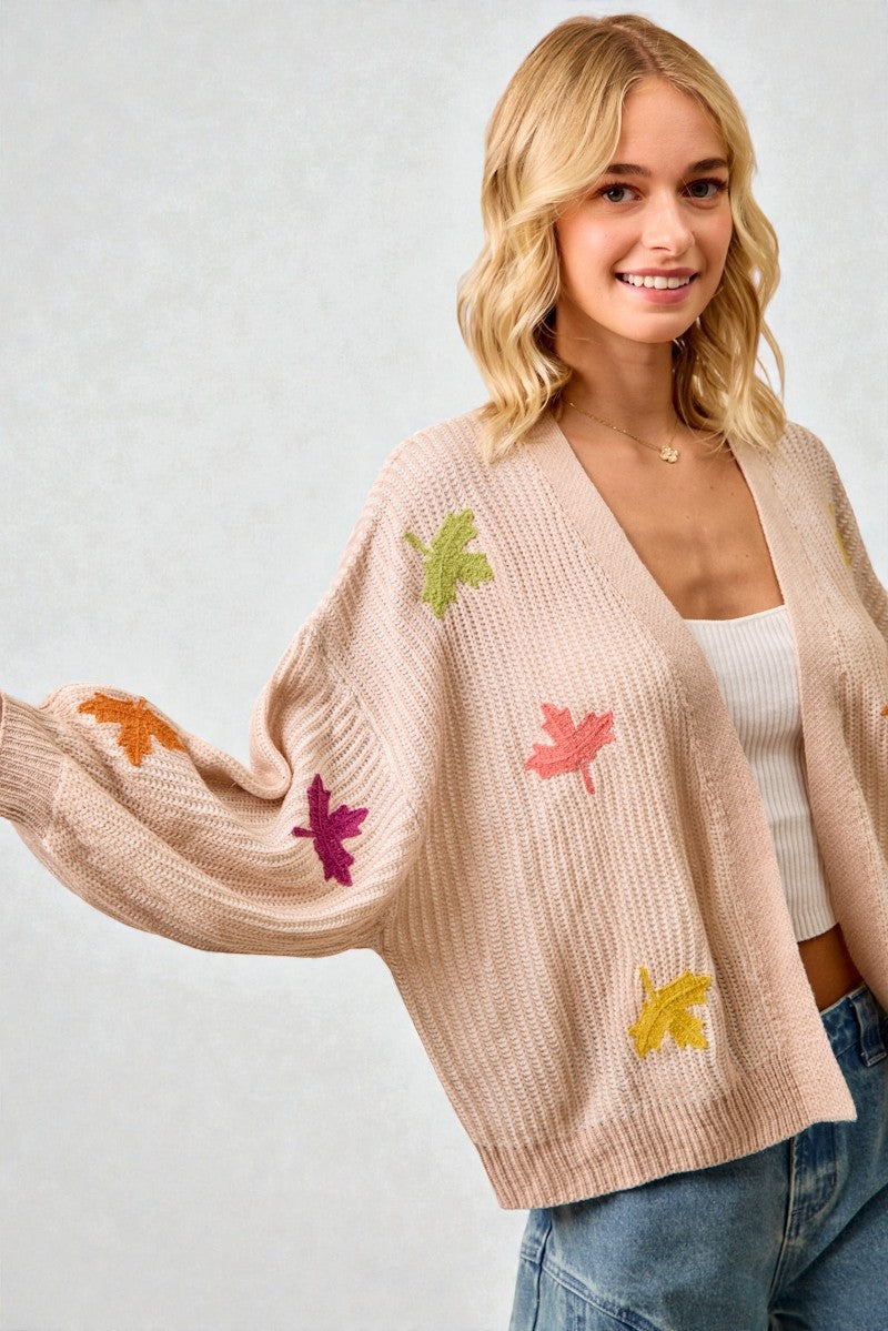 Woman wearing a beige cardigan with colorful leaf patterns on a plain background