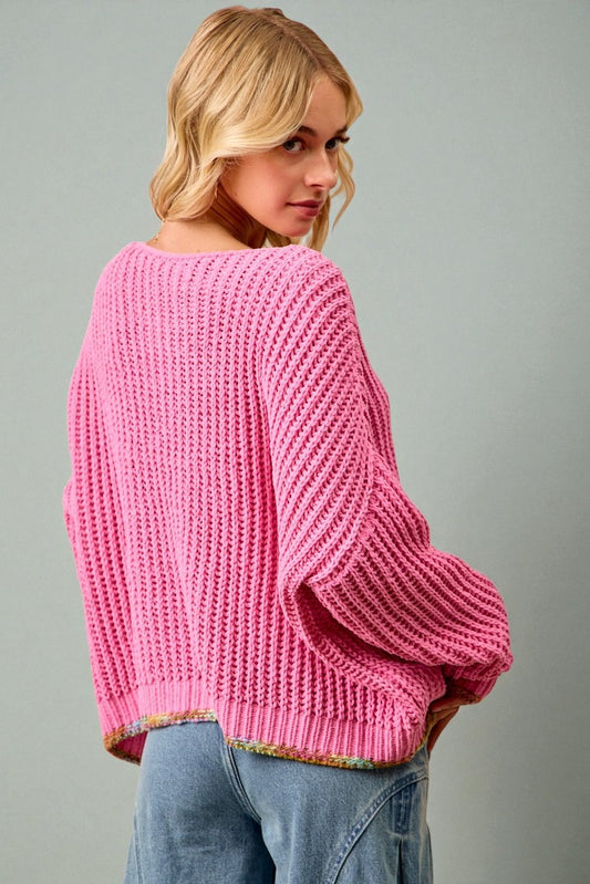 Woman wearing a pink chunky knit sweater against a gray background