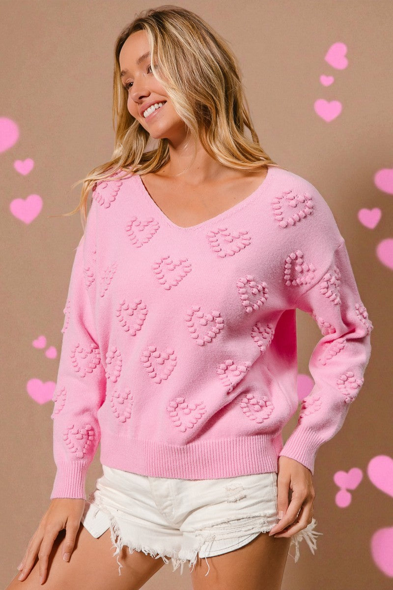 Woman wearing a pink sweater with heart patterns on a beige background with heart shapes.