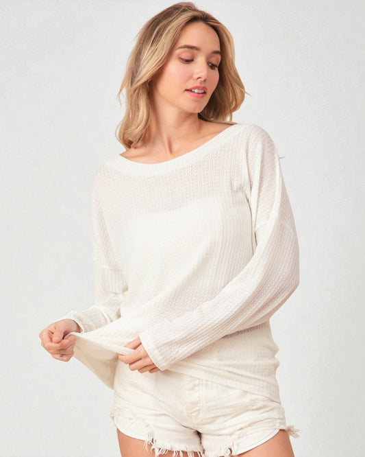 Woman wearing a white ribbed sweater and shorts on a plain background