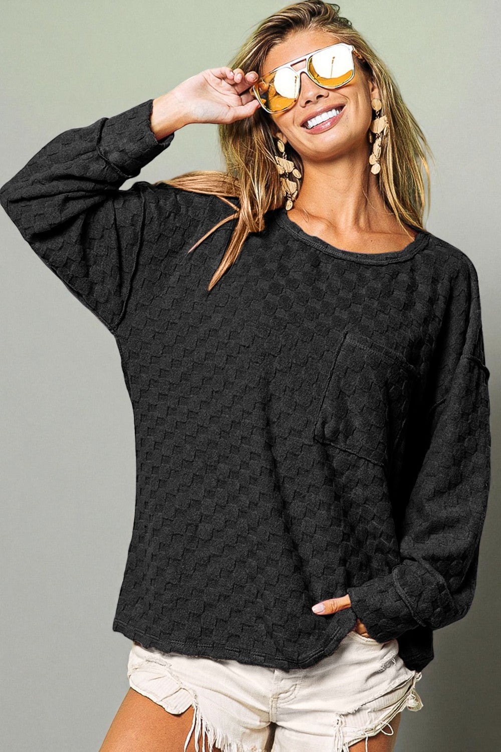 Woman wearing a black textured sweater and white shorts against a gray background