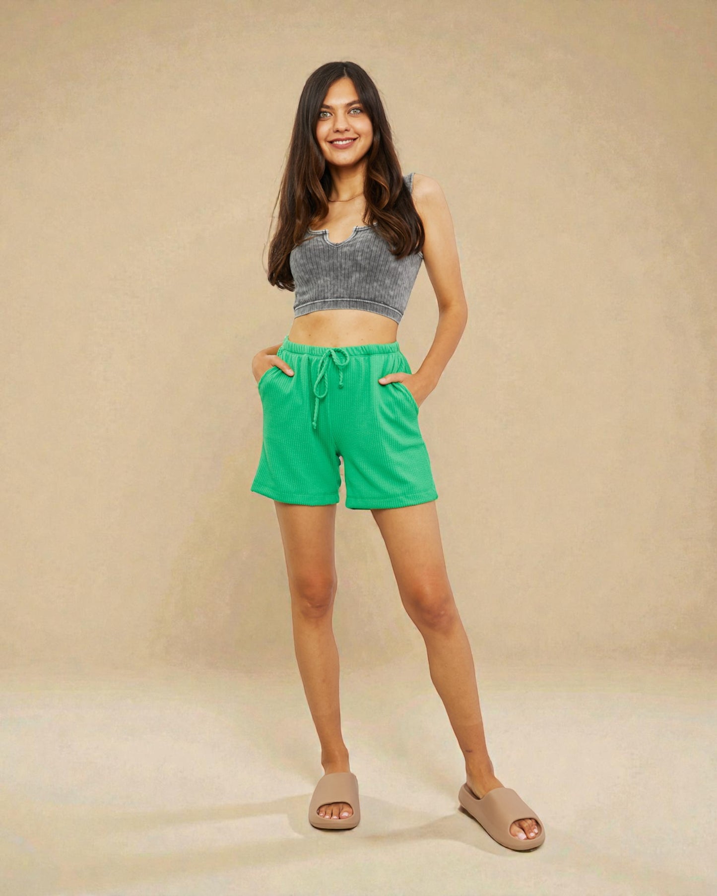 Woman wearing a gray crop top and green shorts on a beige background