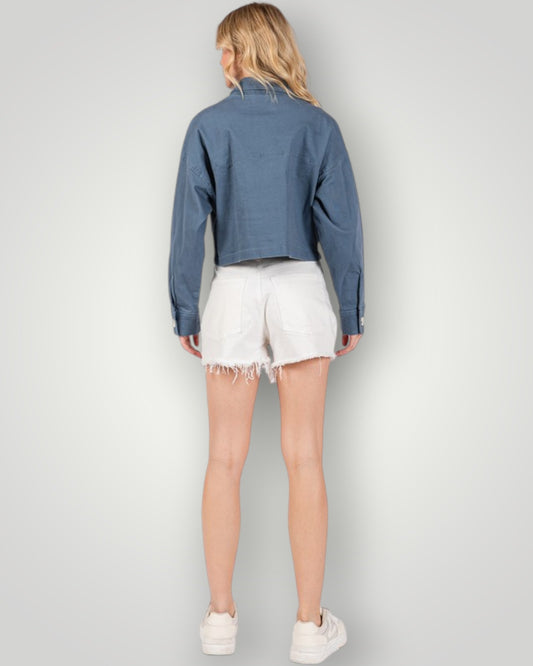 Person wearing a blue denim jacket and white shorts on a plain background