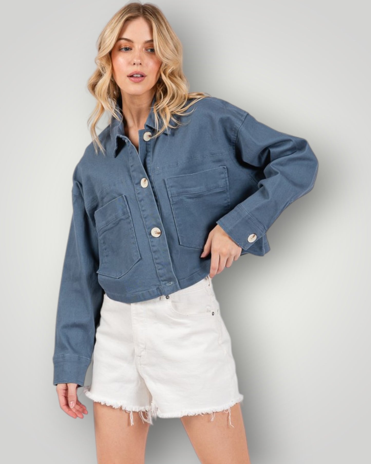 Woman wearing a blue denim jacket and white shorts against a plain background