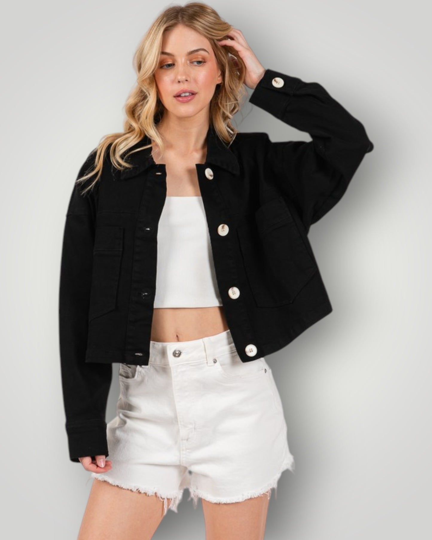 Woman wearing a black jacket, white top, and white shorts on a gray background