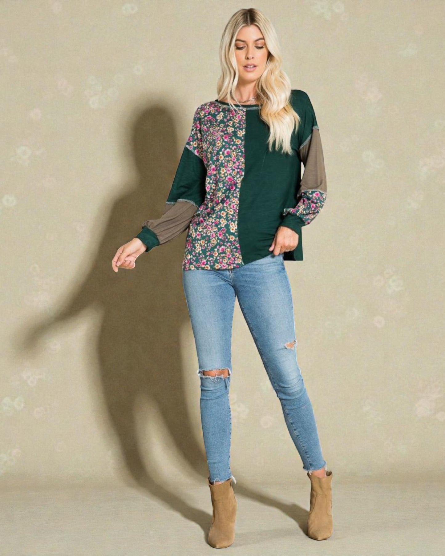Woman wearing a green floral top and blue jeans against a beige background