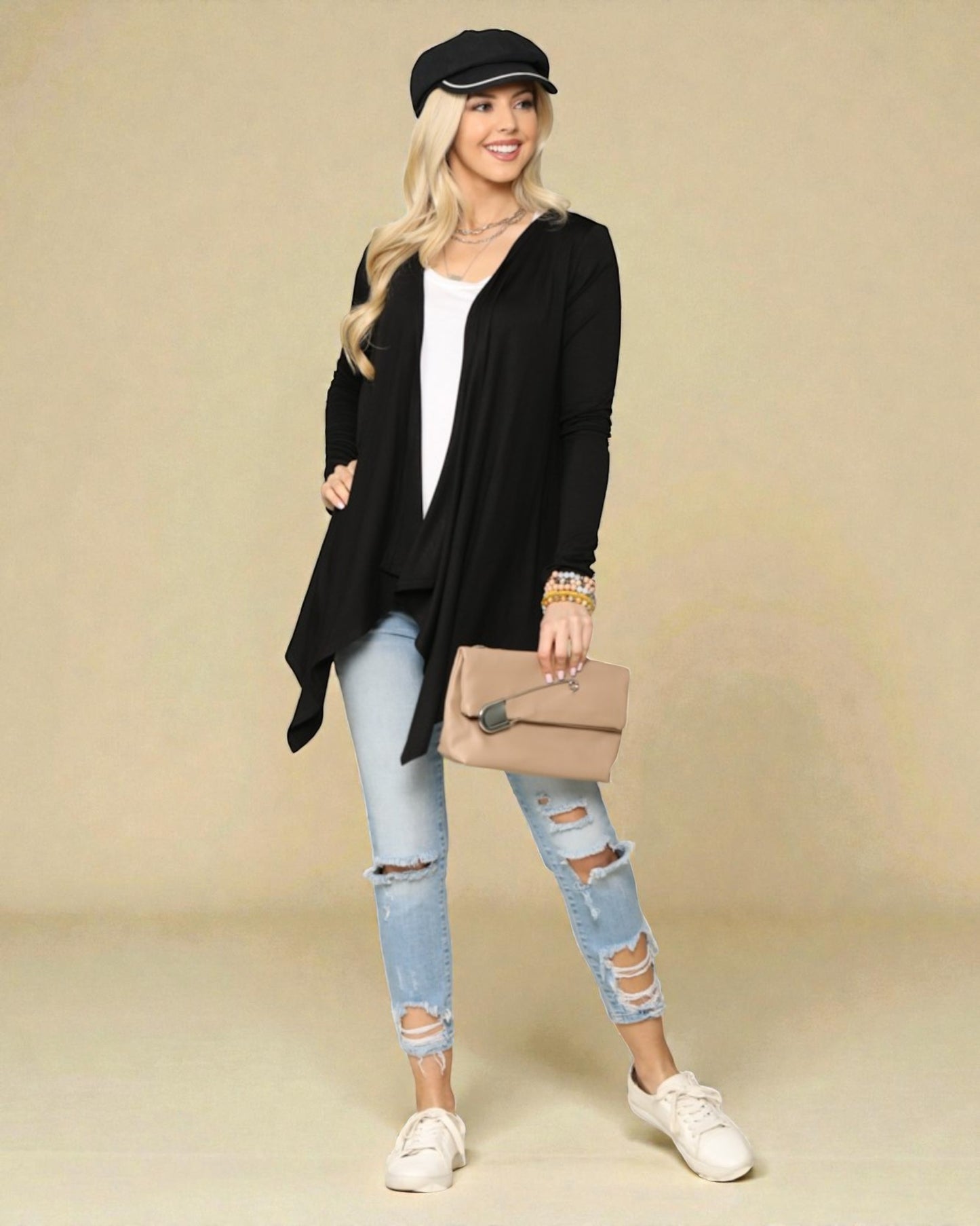 Woman wearing a black cardigan, white top, light blue ripped jeans, and white sneakers on a beige background