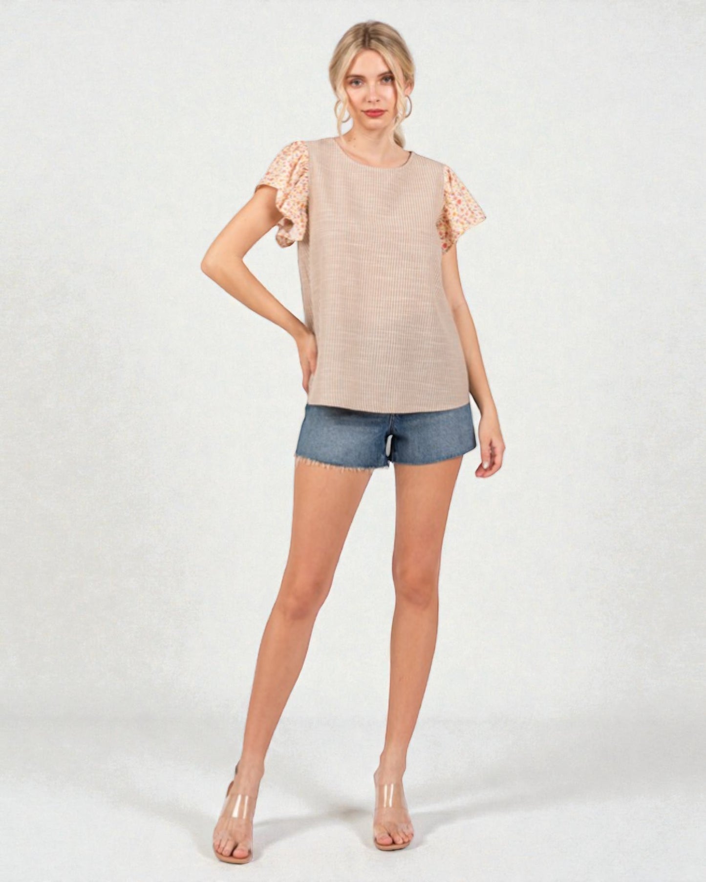 Woman wearing a beige top with lace sleeves and denim shorts on a white background